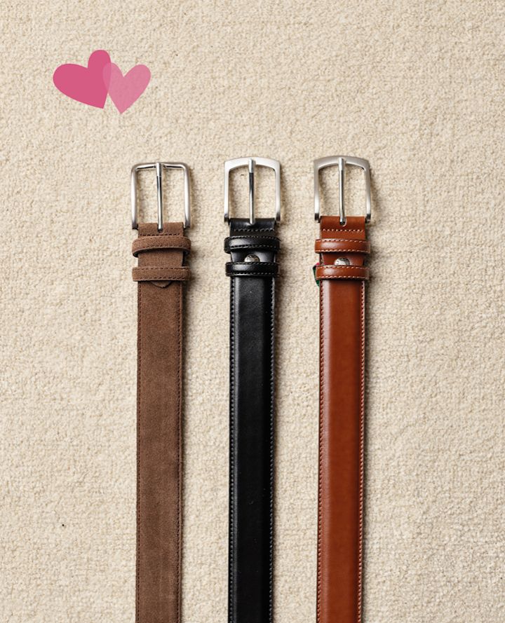 Tre läderbälten i brun, svart och cognac med silverspännen på beige bakgrund, dekorerade med två rosa hjärtan.