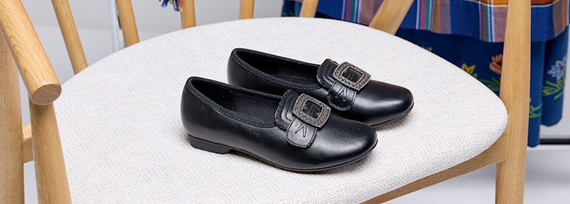 Svart skinnsko med dekorativ spenne plassert på en lys polstret stol med treben.