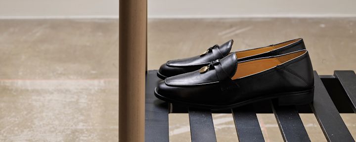 Svart skinnsko med gullfarget dekor på toppen plassert på en svart benk i et rom med betonggulv.