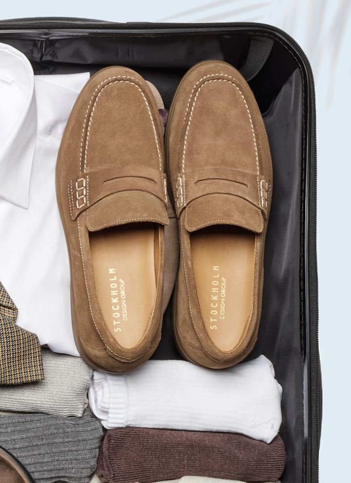 Bruna mocka penny loafers från Stockholm Design Group packade i en resväska med kläder och strumpor.