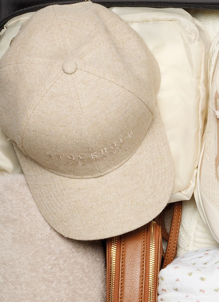 En öppen resväska med beige sneakers, en beige keps, en brun väska och vikta kläder.