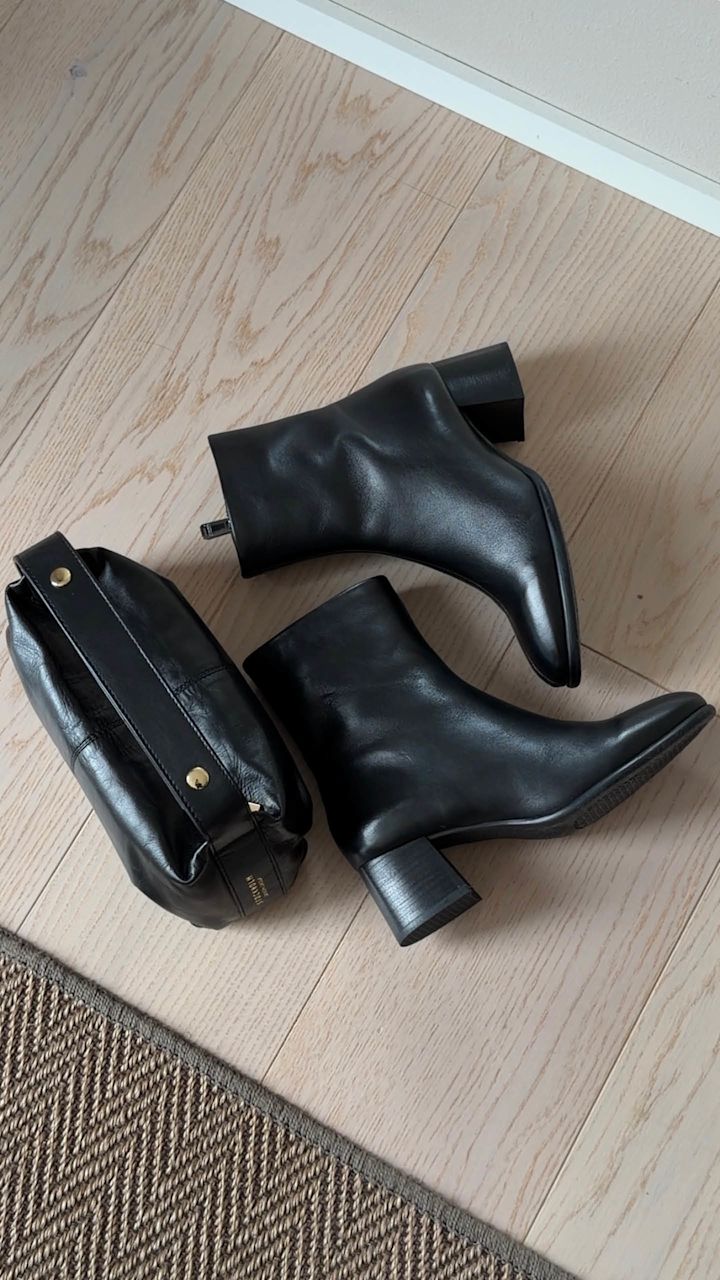 Svarta ankelboots i läder med blockklack och spetsig tå, placerade på ett ljust trägolv.
