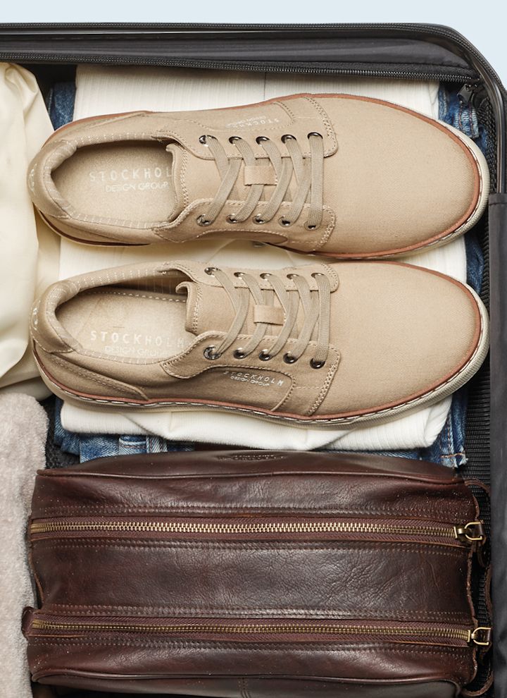 Beige casual sneakers fra Stockholm Design Group pakket i en koffert sammen med klær og en brun lærveske.