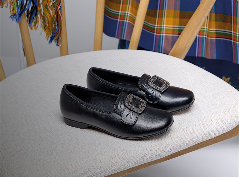 Bunadsko til junior på et hvitt bord med bunad i bakgrunnen.