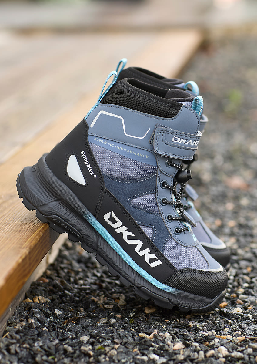 Blå och svart Okaki vinterkänga med turkosa detaljer, robust sula och snörning, placerad på grusunderlag vid träkant.