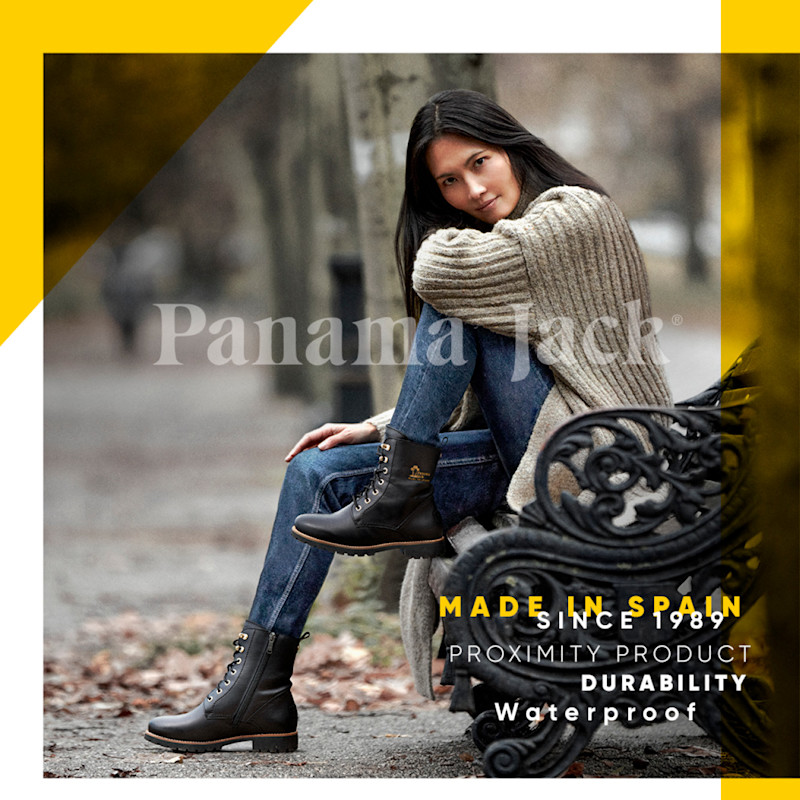 En kvinna sitter på en parkbänk iklädd bruna Panama Jack vattentäta stövlar, blå jeans och en beige stickad tröja i en höstlig utomhusmiljö.