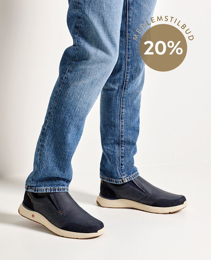 Person iført blå jeans og mørkeblå sko står på hvitt gulv, sirkel med teksten "MEDLEMSTILBUD 20%" vises øverst til høyre.