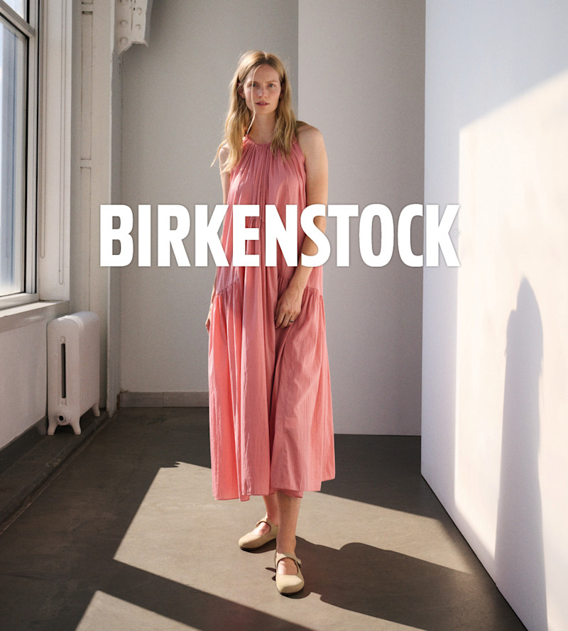 Kvinna i rosa klänning med beige platta Birkenstock-skor med rem över vristen, stilren och minimalistisk look.