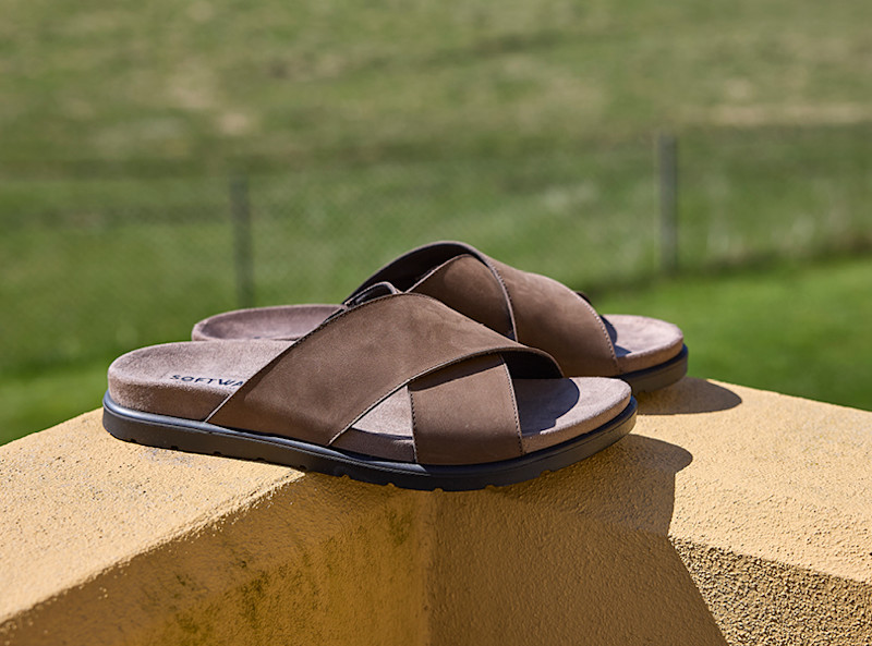 Brune sandaler fra Softwalk i semsket skinn med kryssende stropper og mørk såle, plassert på en gul steinflate utendørs.
