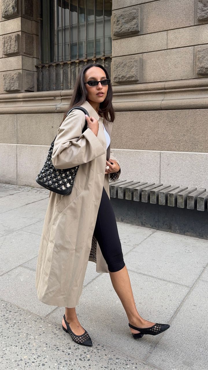 Kvinna i beige trenchcoat och svarta leggings bär svarta spetsiga slingback-ballerinaskor med nätdetaljer och liten klack.