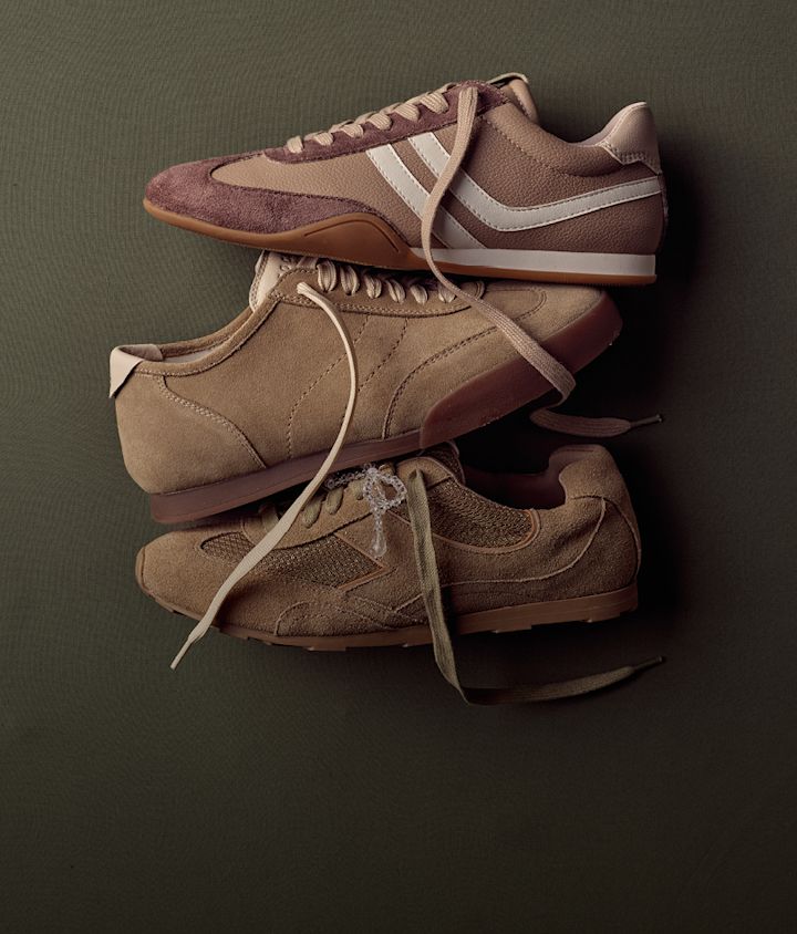 Tre par beiga och bruna retro sneakers i mocka och läder staplade på varandra mot en mörkgrön bakgrund.