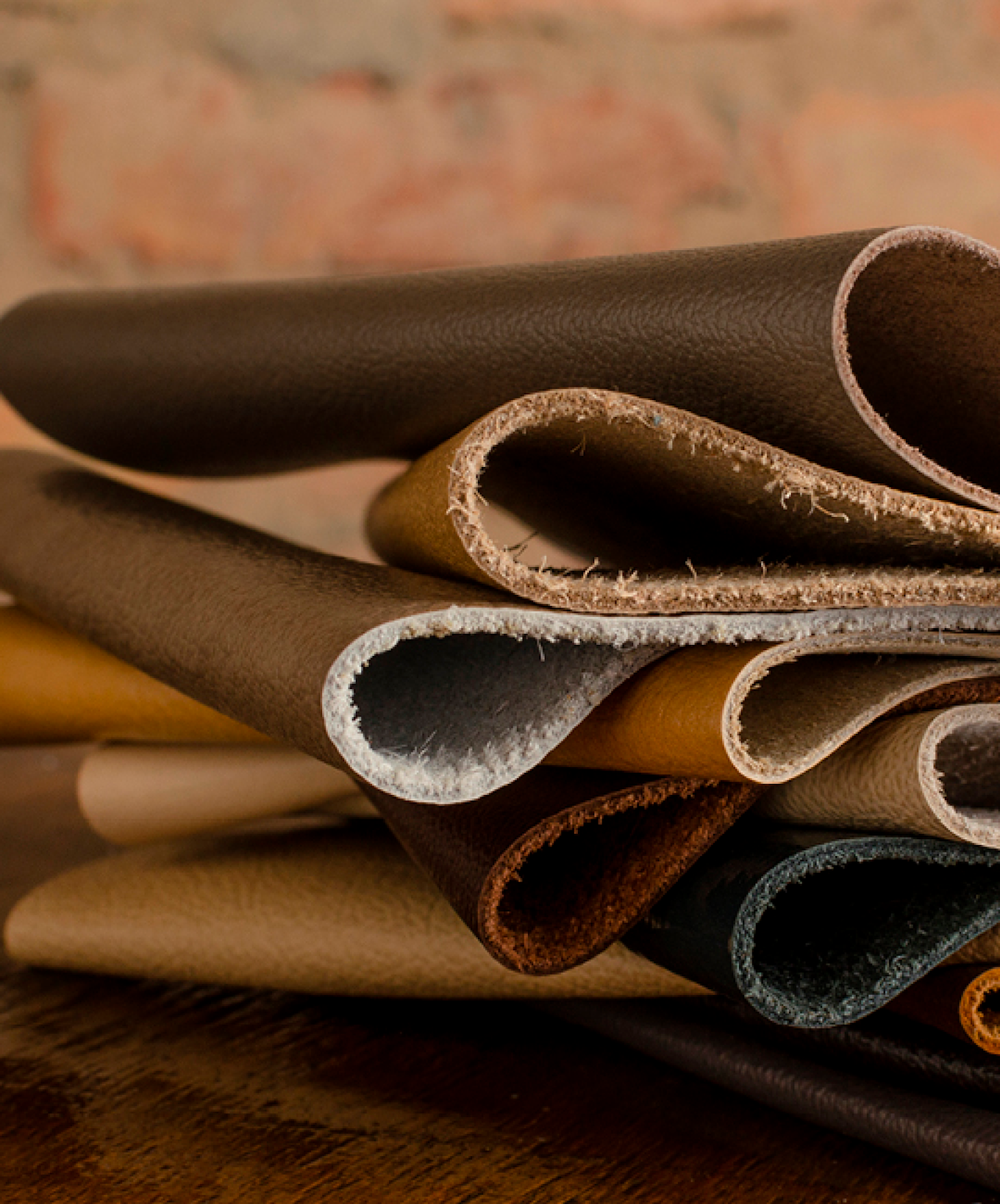 Flera lager av läder i olika bruna och beige nyanser ligger vikta ovanpå varandra på ett träbord.