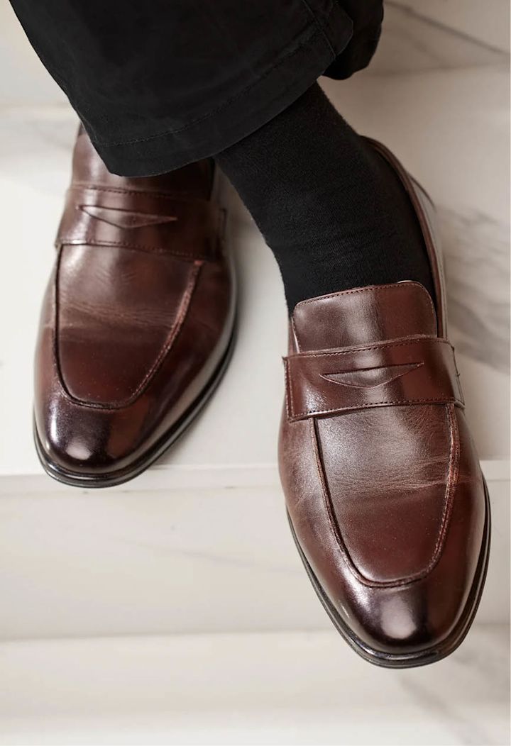 Bruna skinnskor med svarta strumpor och svarta byxben, placerade på vita marmorgolvplattor.