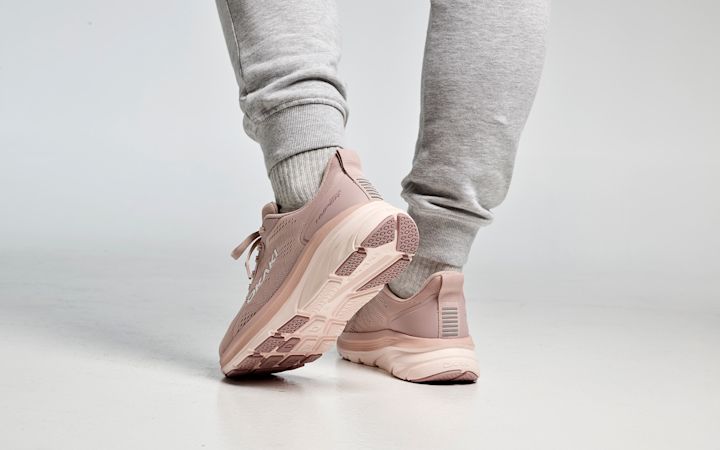 Rosa Hoka-löparskor med hyperdämpning på fötter iförda grå joggingbyxor och strumpor, stående på vit bakgrund.