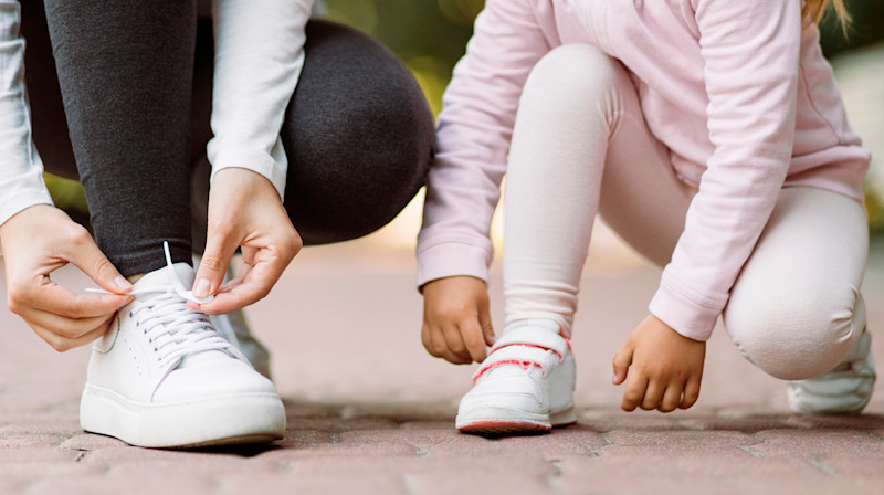 En voksen og et barn knyter skolissene sine mens de er i en utendørs setting på en brosteinsbelagt vei.