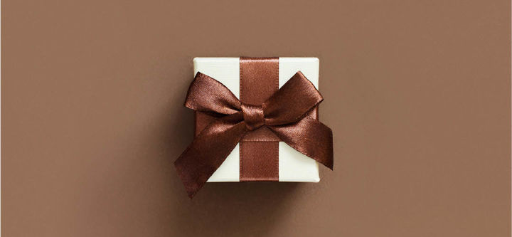 liten hvit gaveeske med brunt bånd på brun bakgrunn