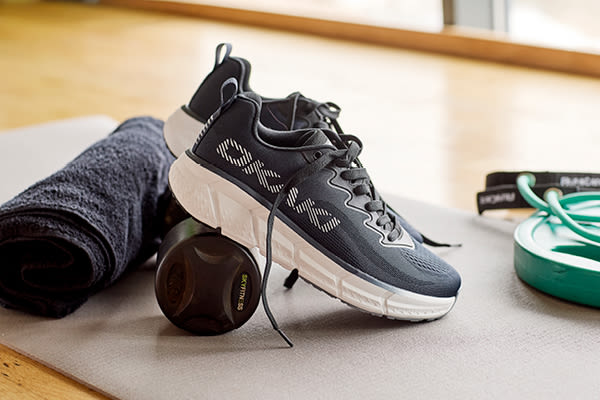 Svarta fritidsskor från Okaki med vit sula bredvid en handduk, träningsredskap och ett grönt hopprep på en träyta.