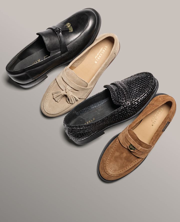 Fire elegante loafers i ulike stiler: svart skinn med spenne, beige semsket med dusk, svart flettet skinn og brun semsket penny-loafer.