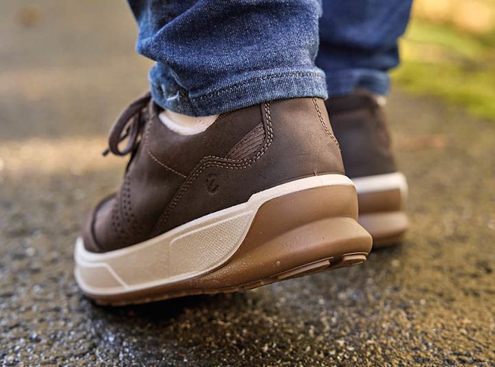 Bruna lädersnörsskor med vit sula, casual sneakerstil, bärs med blå jeans utomhus på asfalt.