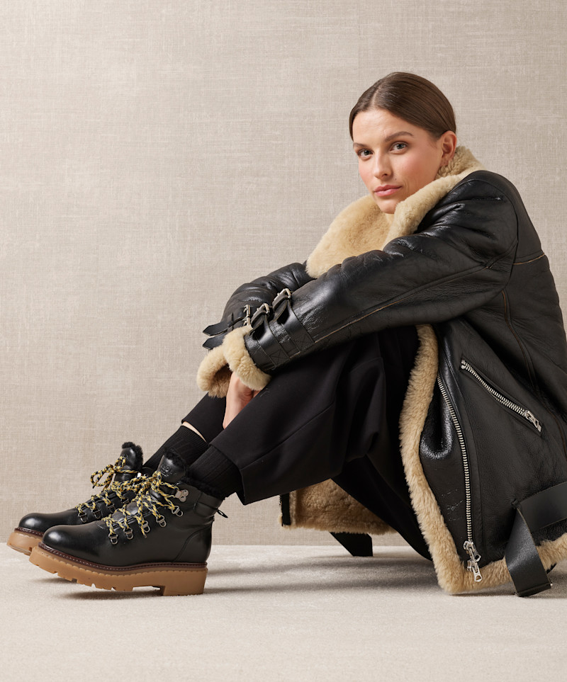 Kvinne sitter på gulvet iført svart skinnjakke med beige fôr og svarte støvler med tykke såler og mønstrede lisser.