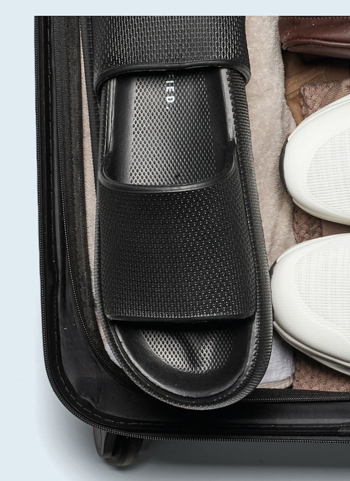 Svarta slippers och vita sneakers packade i en resväska.