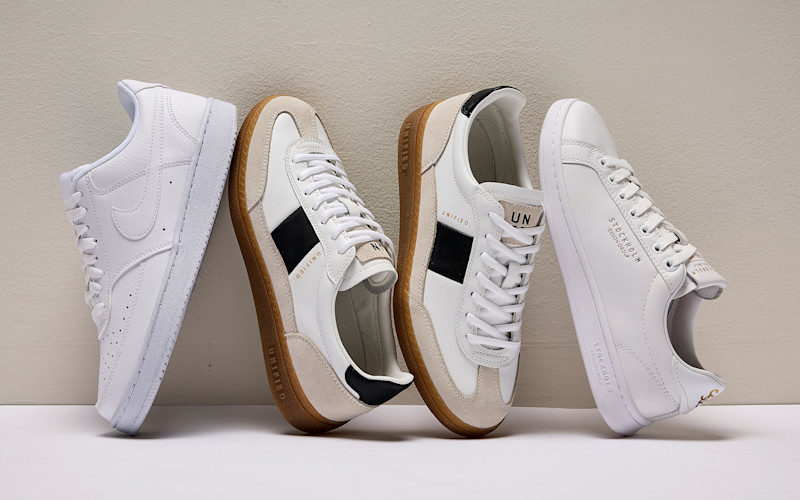 Fyra par vita och beige sneakers står upprätt mot en ljus vägg på en vit yta.