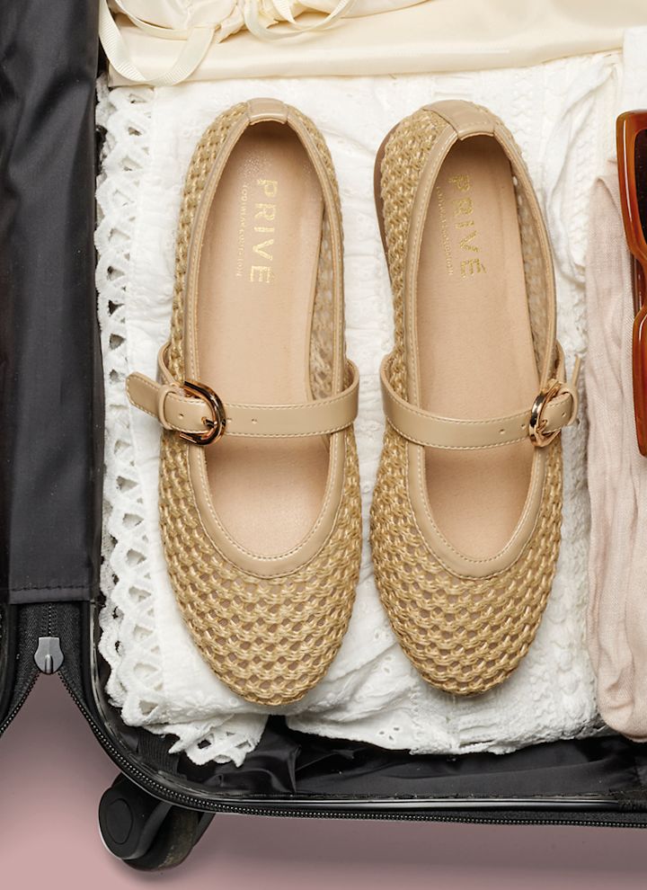 Beige flätade ballerinaskor med guldspänne packade i en resväska med solglasögon och kläder.