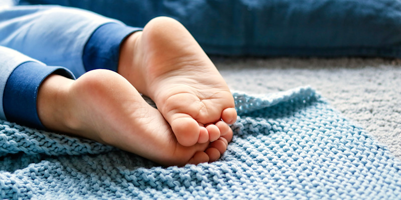Barnfötter som vilar på en blå stickad filt på en ljus matta i en hemmiljö.