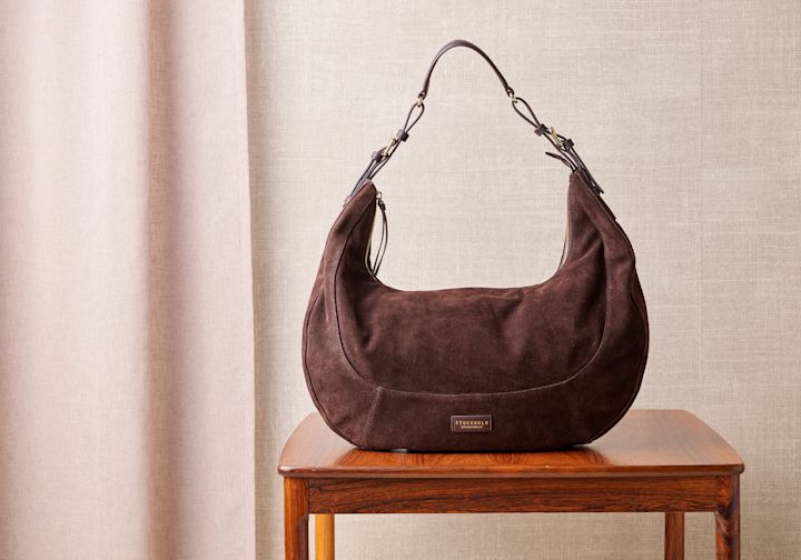 Brun semsket skinnveske fra Stockholm Design Group på et trebord mot en beige bakgrunn.