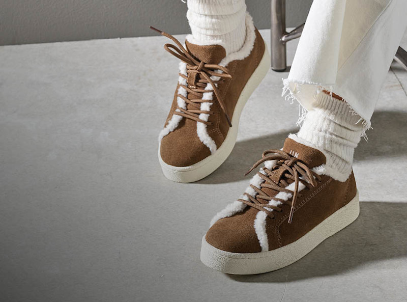 Brune semsket sneakers med hvit shearling-detaljer og kremfarget såle, stylet med hvite sokker og lyse jeans.
