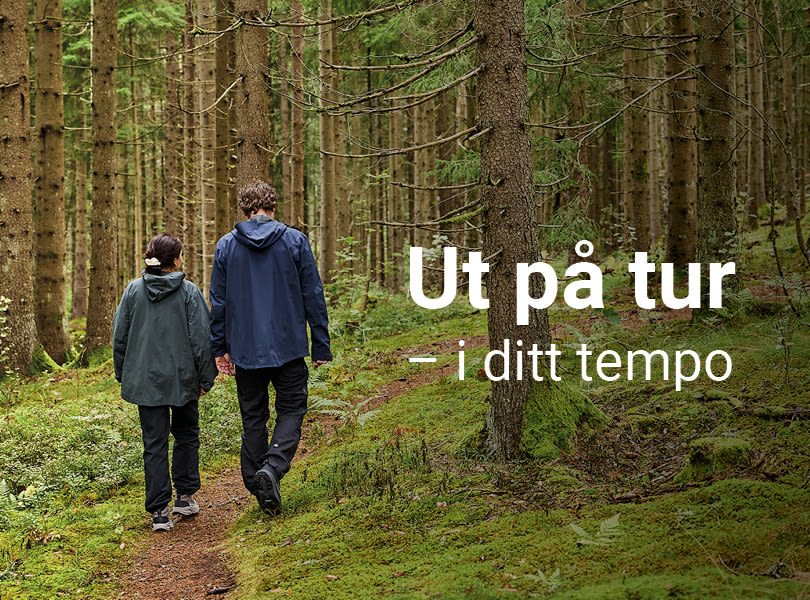 To personer vandrer på en skogsti mellom høye grantrær med tursko fra Okaki. Teksten "Ut på tur - i ditt tempo" vises over bildet.