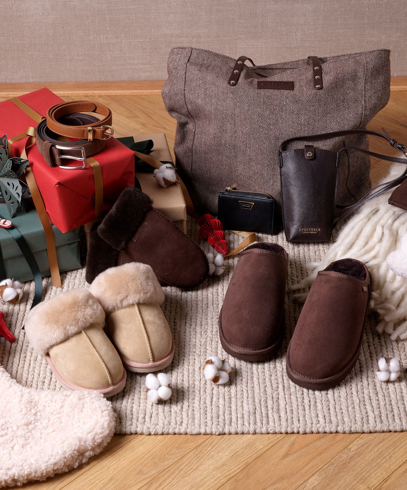 Mysiga tofflor i beige och bruna nyanser med fluffig fårskinnskant, presenterade med väska, plånbok och julklappar på en stickad matta.