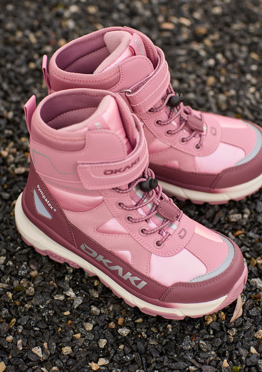 Rosa Okaki kängor för barn med kardborreband och snörning, placerade på grusig mark.