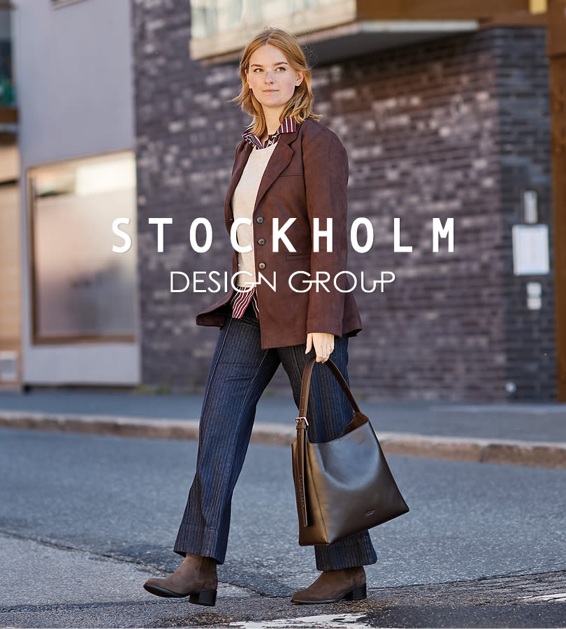 Person i brun blazer og stripete bukser går med brune ankelstøvletter i lær og holder en stor veske, med Stockholm Design Group-logo.