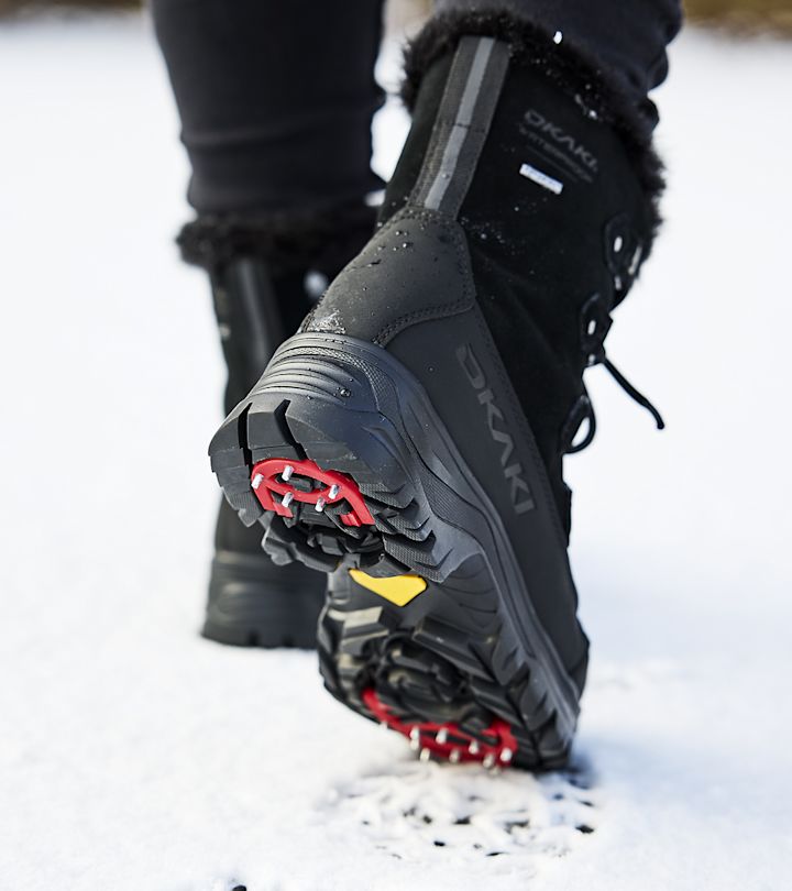 Vinterstövlar med dubbar under sulan som trampar i snö, närbild på baksida och sula.