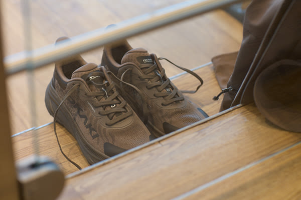 Fritidsskor från Okaki med svarta detaljer placerade på en trätrappa, sedda genom en glasskiva.