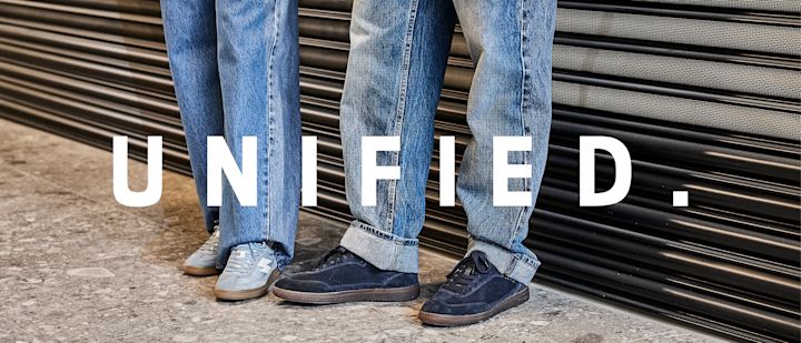 To personer i blå jeans med sneakers - lyseblå og mørkeblå semsket sko med gummisåler. Teksten "UNIFIED." vises i forgrunnen.
