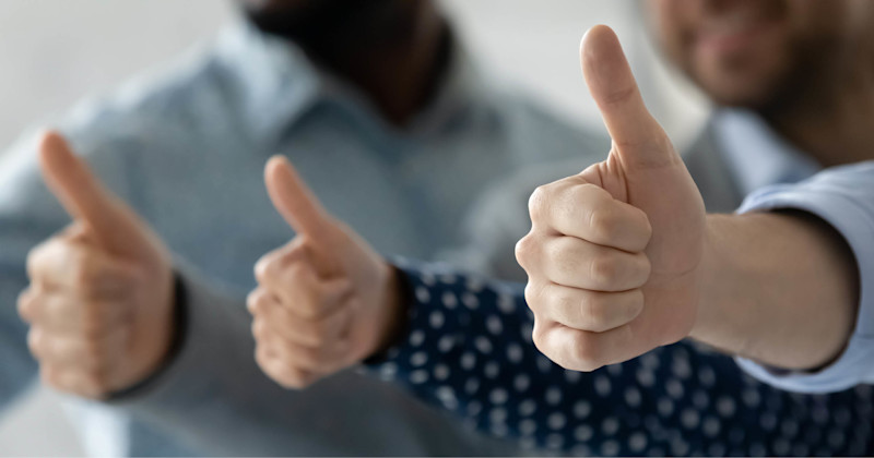 Tre personer ger tummen upp-tecken med utsträckta armar mot en suddig bakgrund.