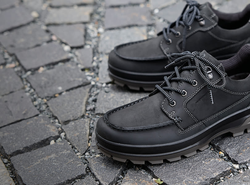 Svarte robuste Ecco Rugged Track herresko med kraftig såle og snøring, plassert på brosteinsunderlag. Medlemstilbud! 20 % på Ecco Rugged Track.
