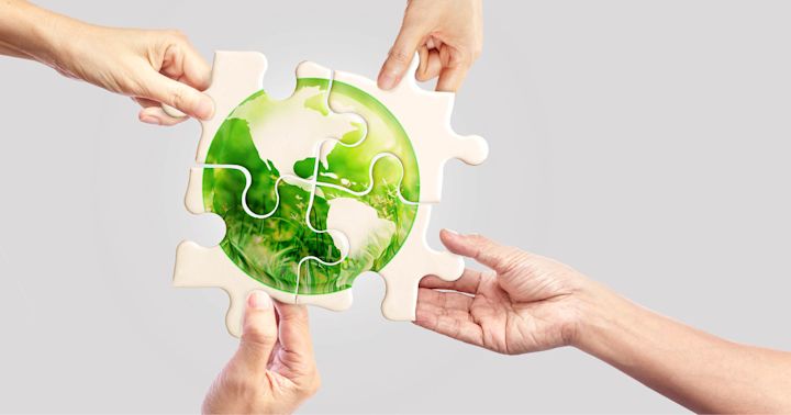 Fire hender som setter sammen et puslespill med jordkloden og grønt gress, symboliserer samarbeid for miljøet.