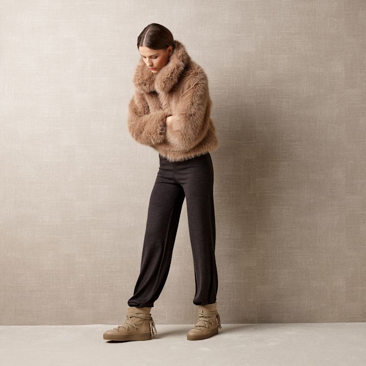 Person i brun pelsjakke og mørke bukser med beige snørestøvler i boots-stil mot nøytral bakgrunn.