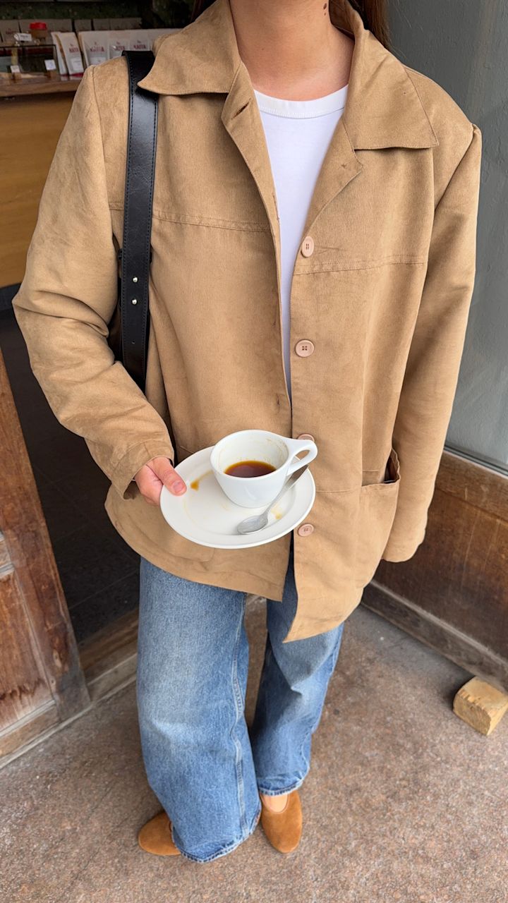 Lisa Alexandra i beige kavaj och jeans bär en kaffekopp och har ljusbruna ballerinaskor från Unified i avslappnad stil.