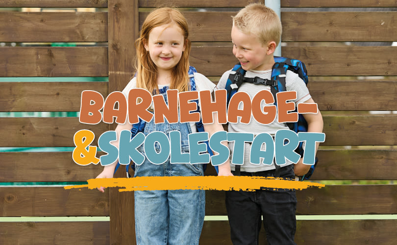 To barn med skolesekker foran trevegg med teksten "BARNEHAGE- &SKOLESTART" i fargerike bokstaver.