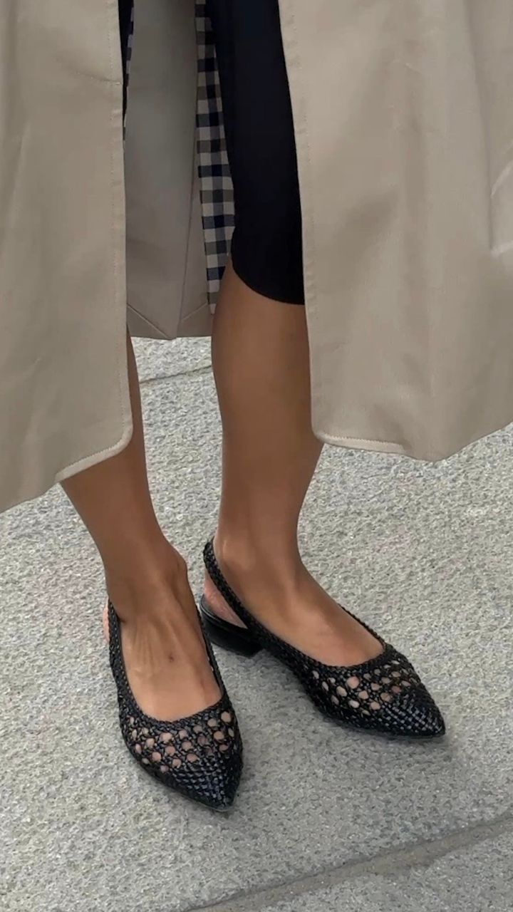 Svarta flätade slingback-ballerinaskor med spetsig tå, låg klack, stilren design. Bärs med beige kappa och svarta leggings.