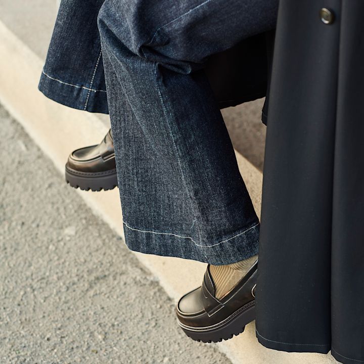 Person i mørke jeans med svarte chunky loafers med kraftig platåsåle og beige sokker.