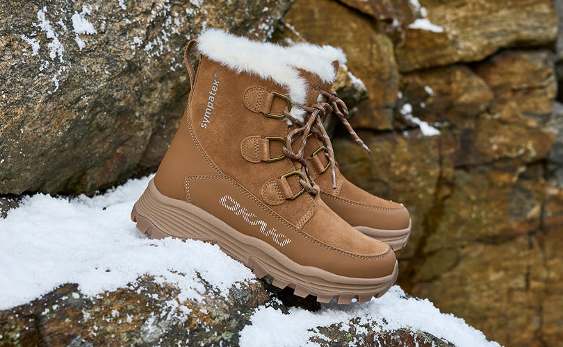 Brun Okaki vintersko med hvit pelskant, snøring og robust såle, plassert på snødekt steingrunn.