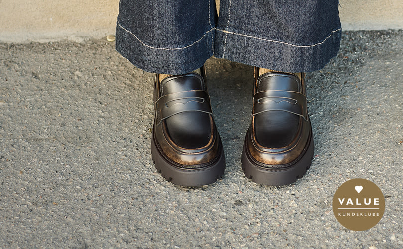 Brune chunky loafers fra Unifiedmed plattformsåle under mørke jeans. VALUE kundeklubb-logo vises i hjørnet.