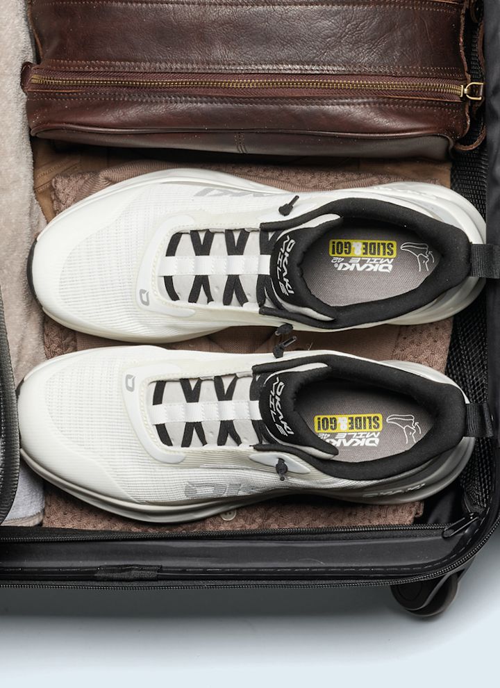Vita sneakers med svarta detaljer packade i en öppen resväska. Sportig stil med svarta skosnören och gula inlägg.