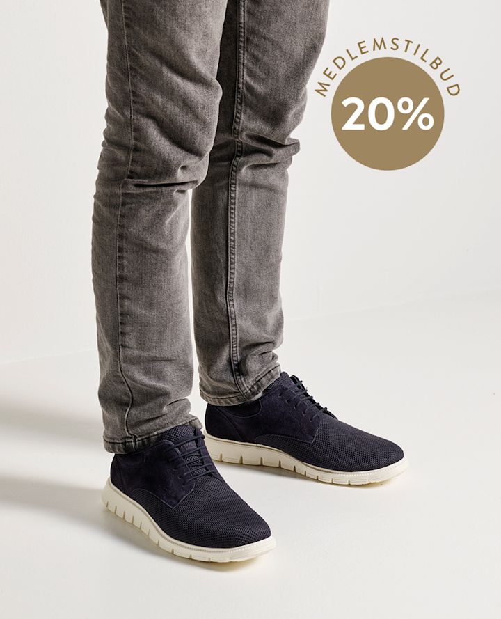 Person med grå jeans har på seg mørkeblå sneakers med hvit såle, sirkel med teksten "MEDLEMSTILBUD 20%" i bakgrunnen.