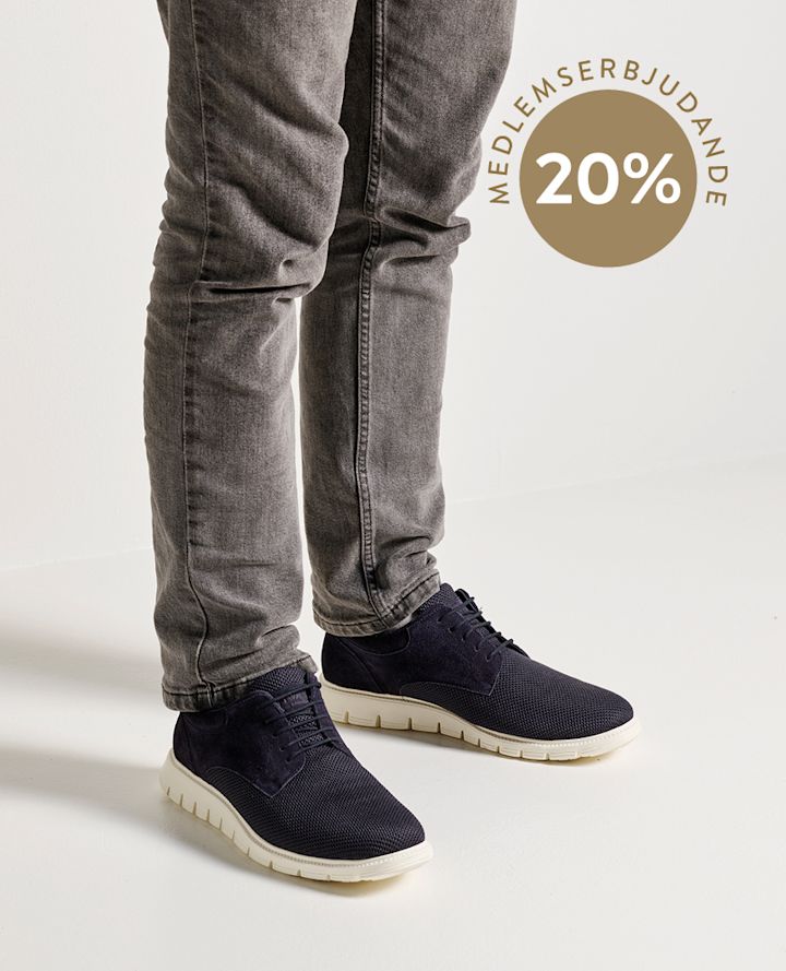 Person med grå jeans har på sig mörkblå sneakers med vit sula, cirkel med texten "MEDLEMSTILBUD 20%" i bakgrunden.